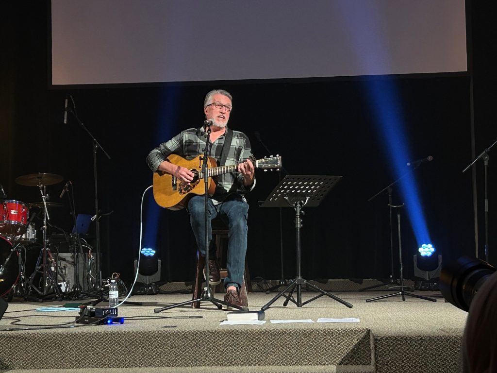 Jordan St. Cyr singing on stage with an acoustic guitar